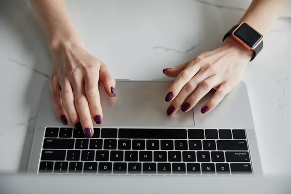 Vista parcial de la mujer en reloj inteligente utilizando el ordenador portátil en la superficie de mármol blanco - foto de stock