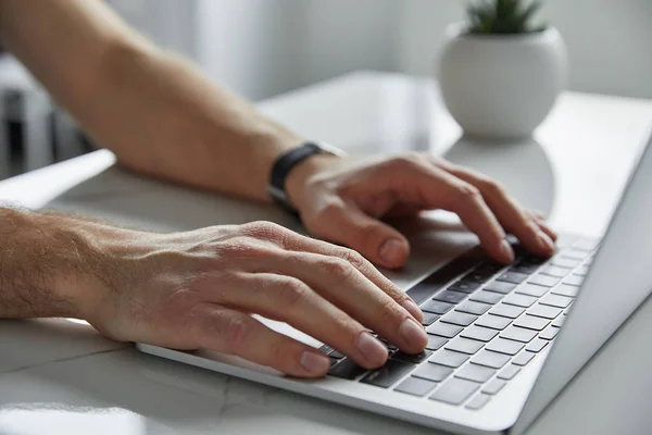 Обрізаний вид людини з ноутбуком з чорною клавіатурою на білому мармуровому столі — стокове фото