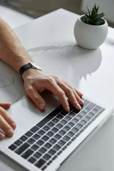 Partial view of man using laptop on on white marble table with flowerpot — Stock Photo