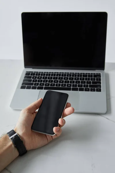 Vista cortada de homem segurando smartphone e laptop com tela em branco isolado em cinza — Fotografia de Stock