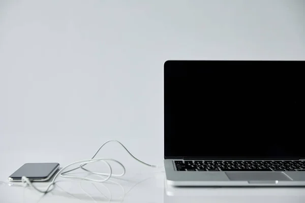 Laptop with blank screen and smartphone with connected earphones isolated on grey — Stock Photo