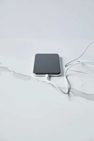 Enfoque selectivo del smartphone con pantalla en blanco con cable conectado aislado en gris - foto de stock