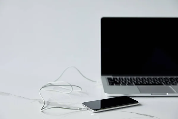 Selective focus of smartphone connected with cable to laptop with blank screen isolated on grey — Stock Photo