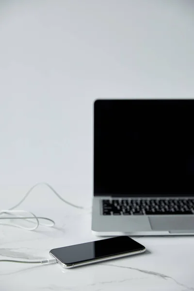Selective focus of smartphone connected to laptop with blank screen isolated on grey — Stock Photo