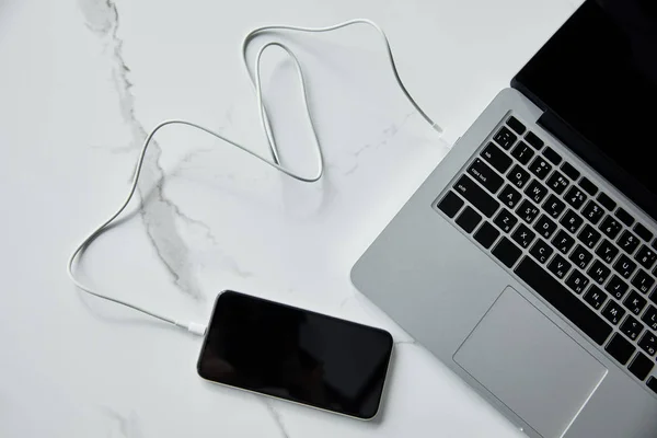 Top view of smartphone with blank screen connected to laptop on white marble surface — Stock Photo