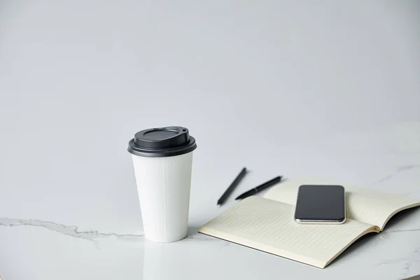 Смартфон з порожнім екраном, блокнот і одноразова чашка ізольовані на сірому — стокове фото