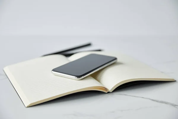 Messa a fuoco selettiva di smartphone con schermo bianco su notebook, penna e matita isolati su grigio — Foto stock