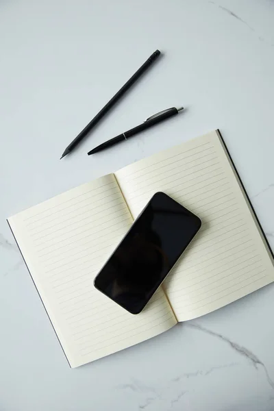 Топ вид смартфона з порожніми екранами, ноутбуками, ручкою і олівцем на білій поверхні мармуру — стокове фото
