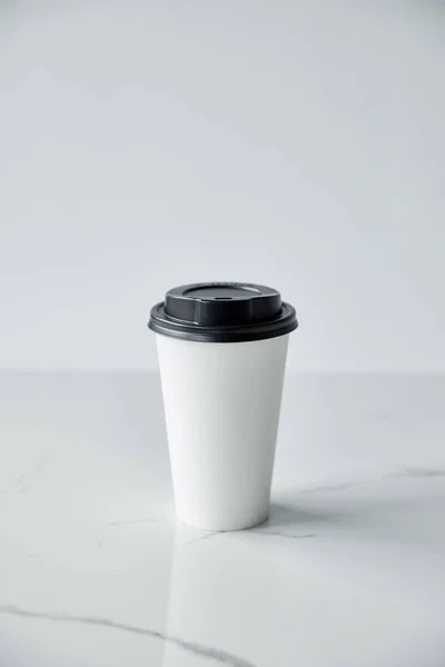 Taza desechable blanco con tapa negra en la superficie de mármol blanco aislado en gris - foto de stock