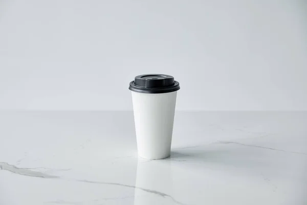 Taza de papel blanco con tapa negra sobre superficie de mármol blanco aislado en gris - foto de stock