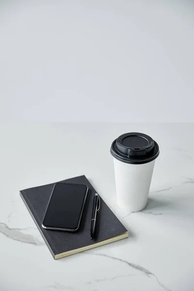 Copo descartável, smartphone com tela em branco, notebook preto e caneta isolada na superfície cinzenta — Fotografia de Stock