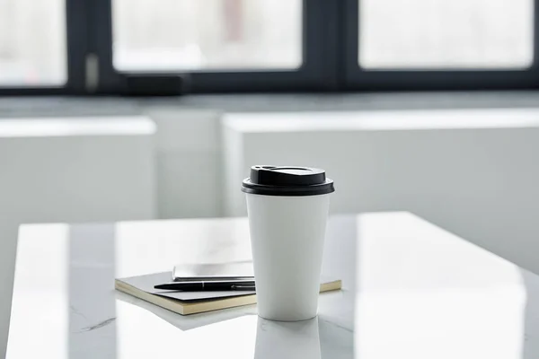 Enfoque selectivo de la taza de papel, cuaderno y pluma en la mesa blanca a la luz del sol — Stock Photo