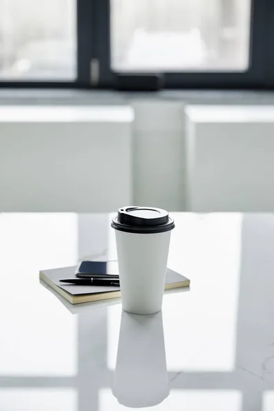 Copo descartável, smartphone com tela em branco, notebook e caneta na mesa branca — Fotografia de Stock