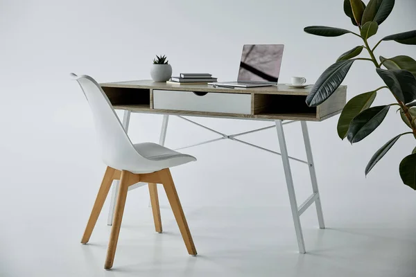 Work table with laptop, books, flowerpot and white chair on grey — Stock Photo