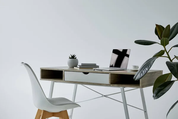 Стол с ноутбуком, книгами, фломастером и белым стулом на сером фоне — стоковое фото