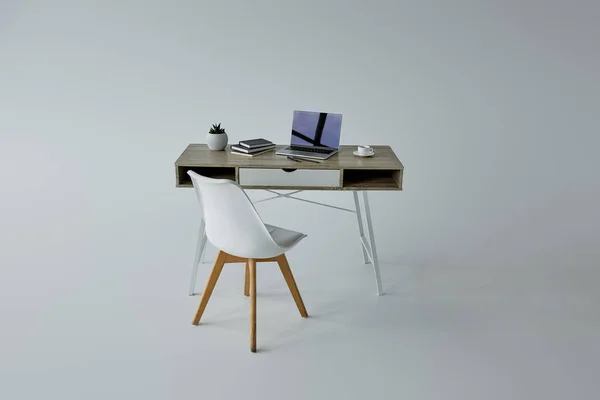 Silla blanca, mesa con libros y portátil sobre fondo gris - foto de stock