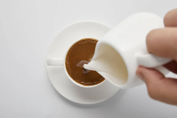 Cropped view of woman pouring milk in coffee on white — Stock Photo