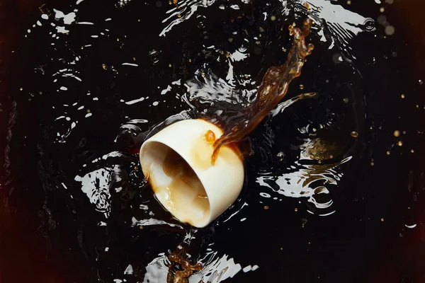 Overturned white porcelain cup with black coffee and splash — Stock Photo