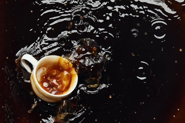 Overturned white porcelain cup with black coffee and splash — Stock Photo