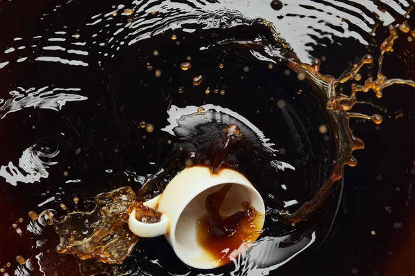 Overturned white porcelain cup with black coffee and splash — Stock Photo