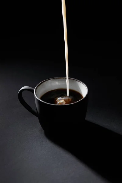 Tasse Kaffee mit eingießender Milch auf dunkel strukturierter Oberfläche — Stockfoto