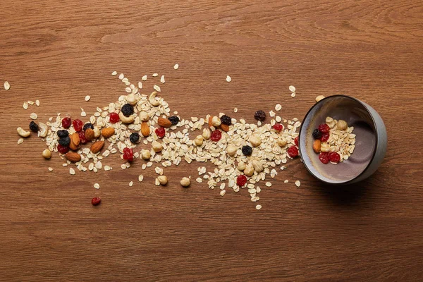 Vista dall'alto di fiocchi d'avena sparsi con noci e bacche secche vicino alla ciotola al tavolo di legno — Foto stock