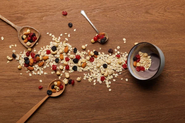 Top view of oat flakes scattered with nuts and dried berries near bowl and spoons at wooden table — Stock Photo
