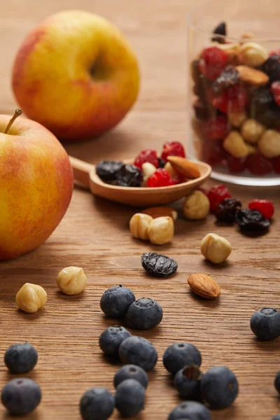 Close up of blueberries and hazelnuts near apples and spoon on wooden table — Stock Photo