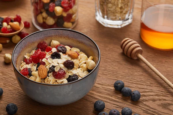Foco selectivo de cereal en tazón con frutos secos y bayas secas preparadas para el desayuno en mesa de madera - foto de stock