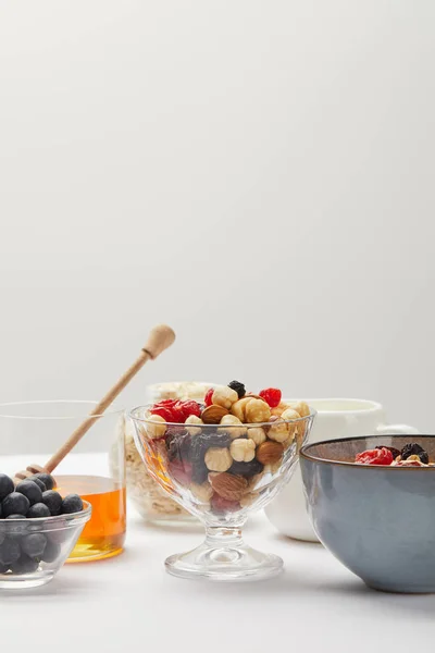 Tazones con bayas, nueces, miel y cereales servidos para el desayuno en mesa blanca aislada en gris - foto de stock