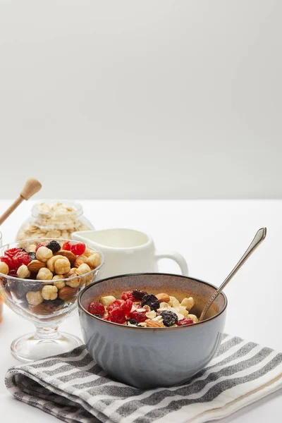 Bowls with berries, nuts, honey and oat flakes served for breakfast on white table isolated on grey — Stock Photo