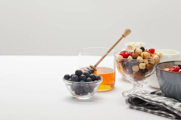 Muesli con bayas, frutos secos y miel servido para el desayuno en mesa blanca aislado en gris - foto de stock