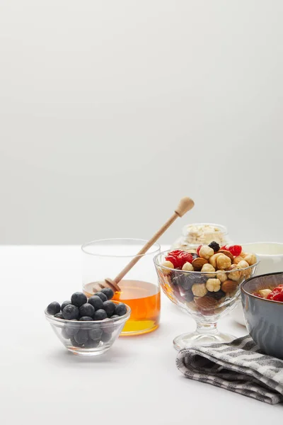 Muesli con bayas, frutos secos y miel en cuencos servidos para el desayuno en mesa blanca aislada en gris - foto de stock