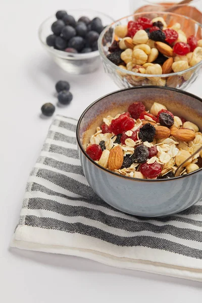 Schüssel auf gestreifter Serviette mit Haferflocken, Nüssen und Beeren auf weißem Tisch — Stockfoto