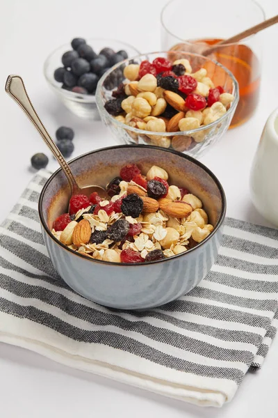 Schüssel auf gestreifter Serviette mit Löffel, Haferflocken, Nüssen und Beeren auf weißem Tisch — Stockfoto