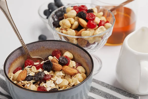 Primer plano del tazón en la servilleta rayada con copos de avena, nueces y bayas en la mesa blanca - foto de stock