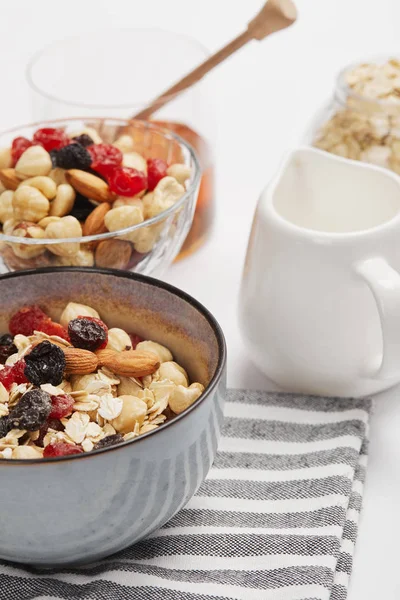 Selective focus of bowl on striped napkin with oat flakes, nuts and berries near white milk jug — Stock Photo