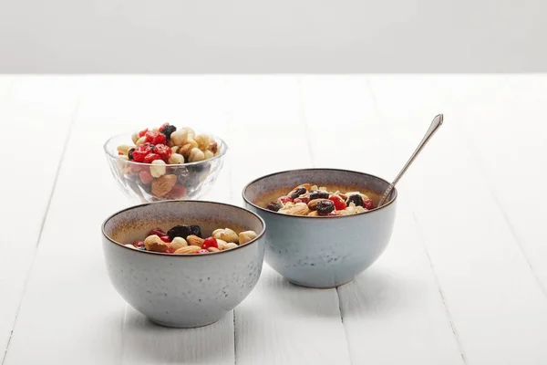 Tazones con muesli, bayas secas y frutos secos servidos para el desayuno en mesa blanca aislada en gris - foto de stock