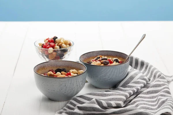 Bowls with muesli, dried berries and nuts served for breakfast near striped napkin isolated on blue — Stock Photo