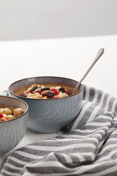 Bowls with muesli, dried berries and nuts served for breakfast near striped cloth isolated on grey — Stock Photo