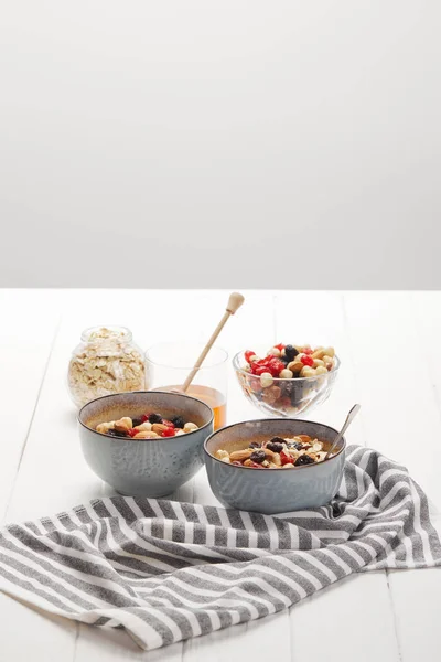 Taças com muesli, bagas secas e nozes servidas ao pequeno-almoço com mel isolado em cinzento — Fotografia de Stock