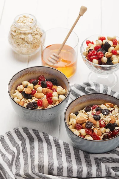 Ciotole con muesli, bacche secche e noci servite a colazione con miele sul tavolo di legno bianco — Foto stock