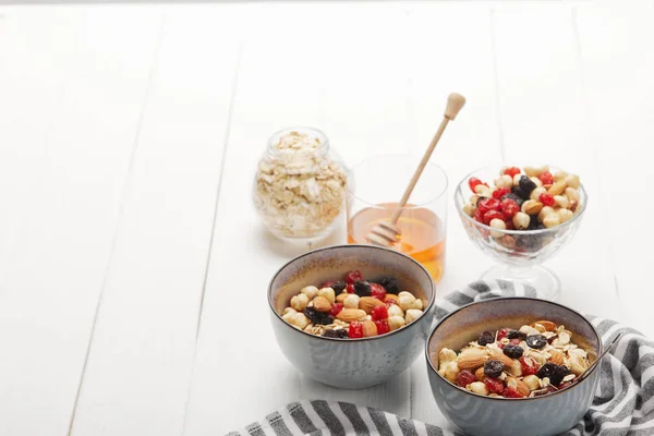 Bowls with muesli, dried berries and nuts served for breakfast with honey on white wooden table with copy space — Stock Photo