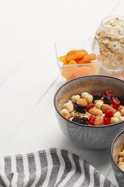 Ciotole con muesli, bacche secche e noci servite per colazione con albicocche secche su tavolo in legno bianco con spazio copia — Foto stock