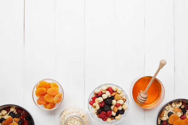 Top view of bowls with cereal, dried apricots and berries, honey and nuts on white table — Stock Photo