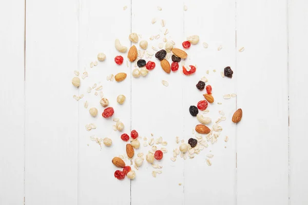 Draufsicht auf verstreute getrocknete Beeren, Haferflocken und Nüsse auf weißem Holztisch — Stockfoto