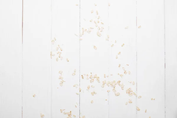 Vista superior de flocos de aveia espalhados na mesa de madeira branca — Fotografia de Stock