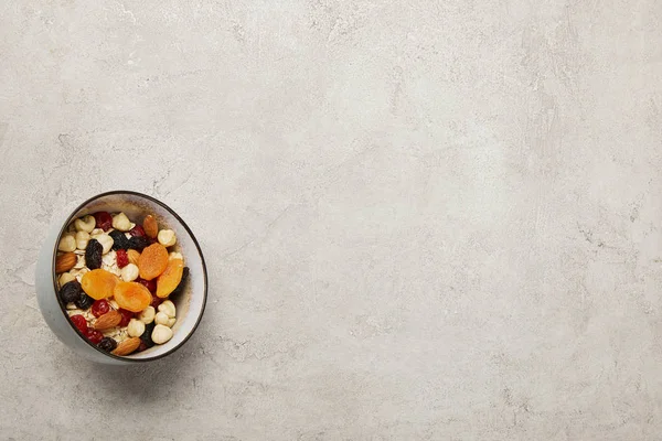 Вид зверху миски з мюслі, сушеними абрикосами та ягодами, горіхами на текстурованій сірій поверхні — Stock Photo