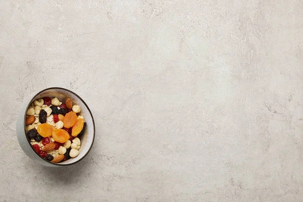 Vista dall'alto della ciotola con muesli, albicocche secche e bacche, noci su superficie grigia testurizzata — Foto stock