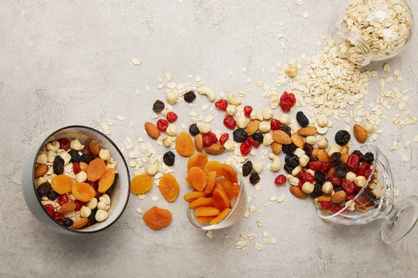 Top view of bowls with muesli, dried apricots and berries, nuts on textured grey surface with messy scattered ingredients — Stock Photo